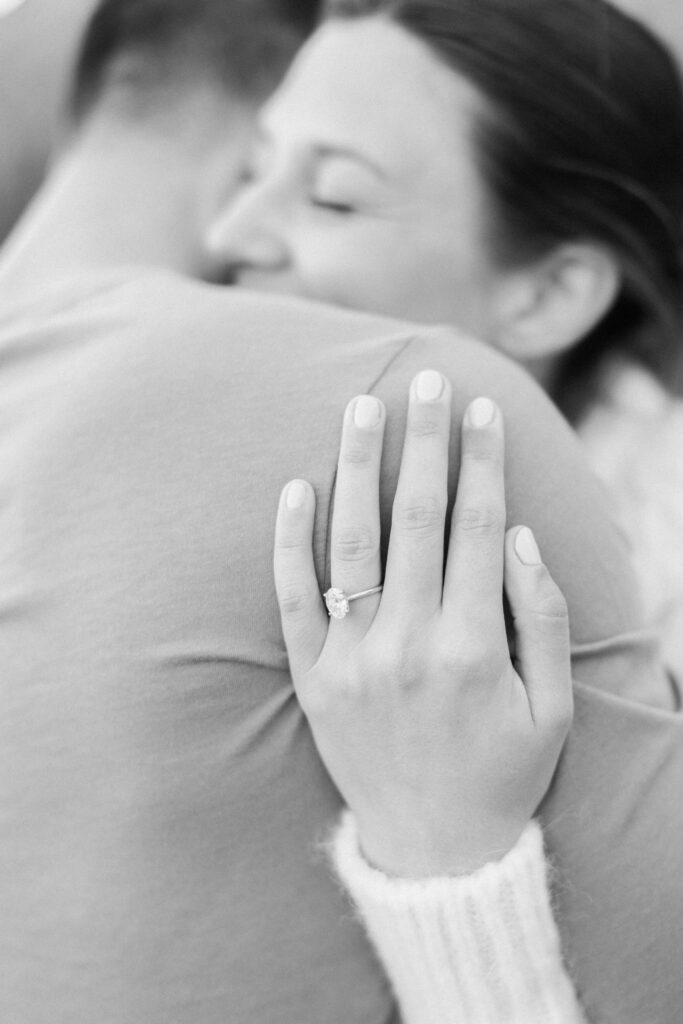 A woman smiles with her eyes closed while hugging someone, displaying an engagement ring on her left hand. The photo is in black and white, and her fingernails are neatly manicured. Copyright - Lisa Leanne Photography, California