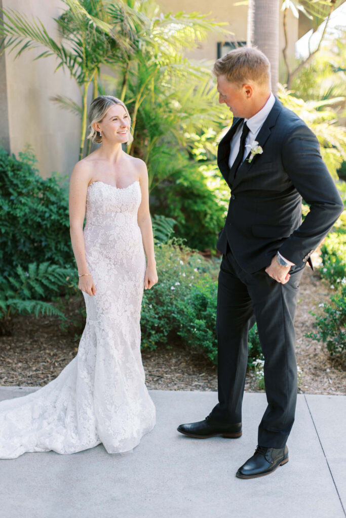 Malibu-Estate-Wedding_Malibu-Wedding_Southern-California-Wedding-Photographer_Lisa-Leanne-Photography_11-683x1024 A bride in a strapless lace gown smiles at a groom in a dark suit as they stand outside surrounded by greenery and sunlight. Copyright - Lisa Leanne Photography, California