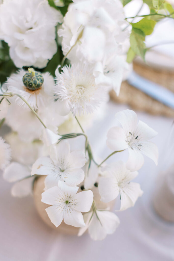 Malibu-Estate-Wedding_Malibu-Wedding_Southern-California-Wedding-Photographer_Lisa-Leanne-Photography_59-683x1024 A close-up of a floral arrangement with delicate white flowers and greenery, softly lit, creating an elegant and fresh atmosphere on a white tablecloth. Copyright - Lisa Leanne Photography, California