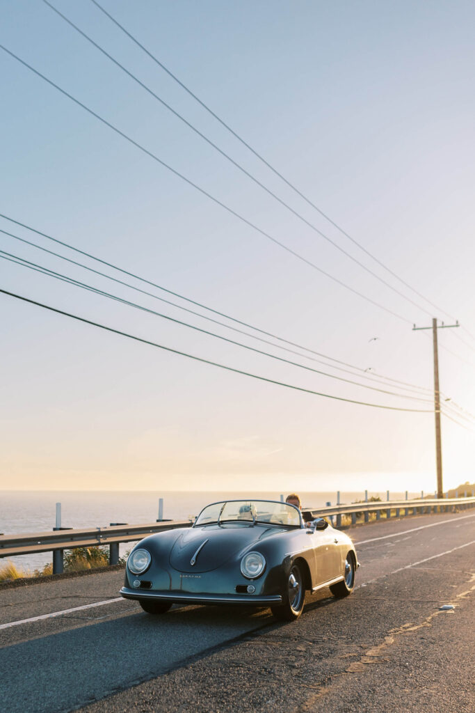 Malibu-Estate-Wedding_Malibu-Wedding_Southern-California-Wedding-Photographer_Lisa-Leanne-Photography_65-683x1024 A classic convertible car drives along a coastal road at sunset with power lines overhead, the ocean on one side, and a clear sky in the background. Copyright - Lisa Leanne Photography, California