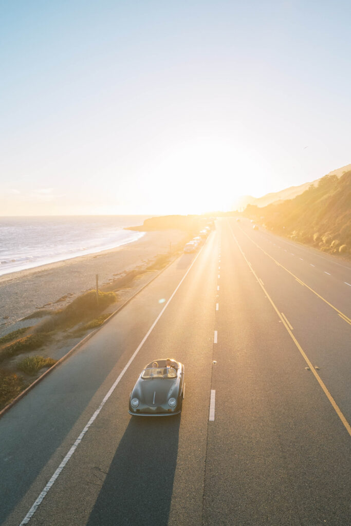 Malibu-Estate-Wedding_Malibu-Wedding_Southern-California-Wedding-Photographer_Lisa-Leanne-Photography_67-683x1024 A classic convertible car drives along a coastal highway at sunset, with golden sunlight illuminating the empty road, sandy beach, and ocean on the left. Copyright - Lisa Leanne Photography, California