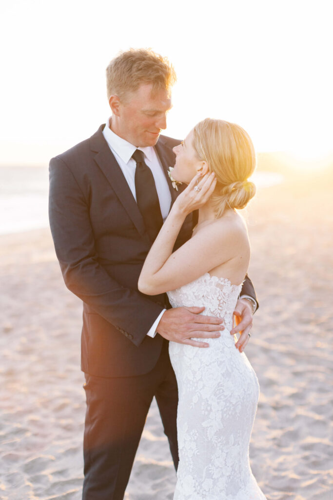 Malibu-Estate-Wedding_Malibu-Wedding_Southern-California-Wedding-Photographer_Lisa-Leanne-Photography_72-683x1024 A bride and groom embrace on a sandy beach at sunset. The groom wears a black suit and tie, and the bride wears a white lace strapless gown. They look into each other's eyes, softly lit by the golden sunlight. Copyright - Lisa Leanne Photography, California