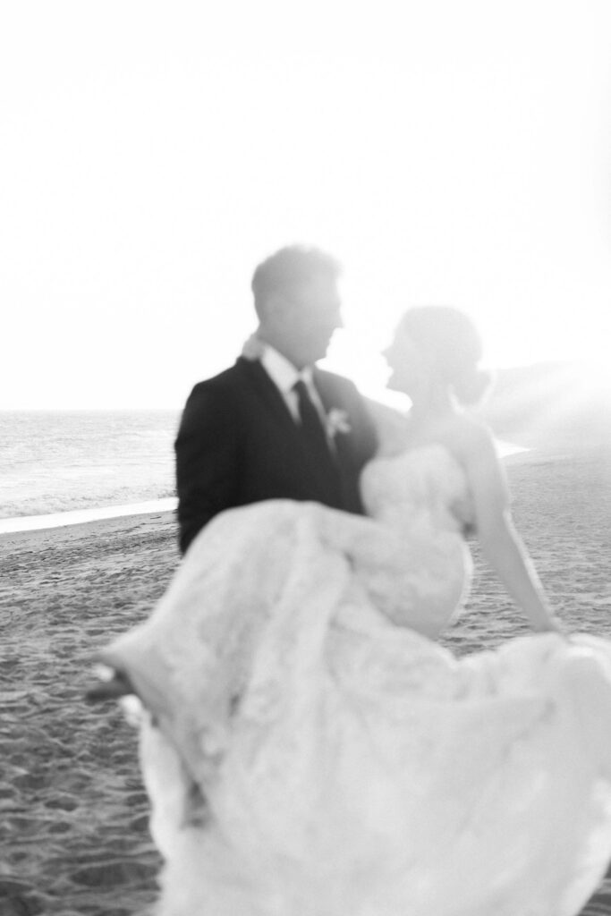 Malibu-Estate-Wedding_Malibu-Wedding_Southern-California-Wedding-Photographer_Lisa-Leanne-Photography_75-683x1024 A bride in a strapless gown is being carried by a groom in a suit along a beach, with sunlight creating a dreamy, soft-focus effect. Copyright - Lisa Leanne Photography, California