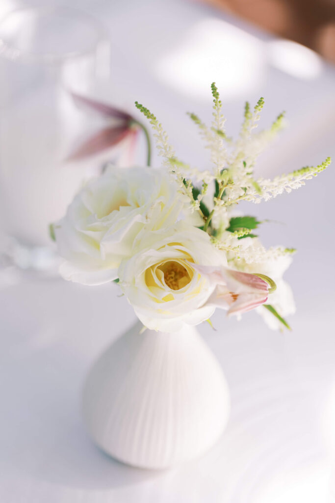 San-Ysidro-Ranch-Rehearsal-Dinner_Santa-Barbara-Wedding_Southern-California-Wedding-Photographer_Lisa-Leanne-Photography_10-683x1024 A small white vase holding white roses, delicate white flowers, and greenery, set on a soft, light background. The arrangement appears elegant and simple. Copyright - Lisa Leanne Photography, California