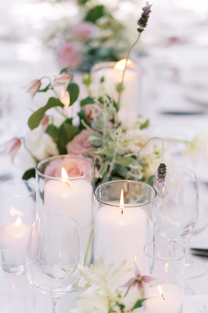 San-Ysidro-Ranch-Rehearsal-Dinner_Santa-Barbara-Wedding_Southern-California-Wedding-Photographer_Lisa-Leanne-Photography_28-683x1024 A close-up of a table centerpiece with white candles in glass holders, surrounded by soft pink and white flowers and greenery, creating an elegant and romantic atmosphere. Copyright - Lisa Leanne Photography, California