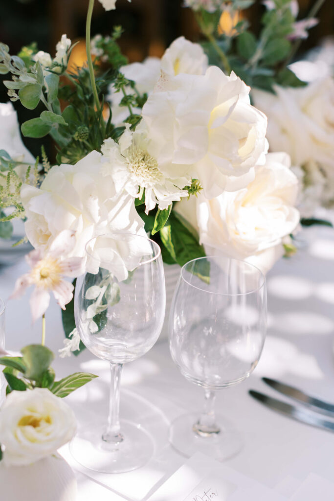 San-Ysidro-Ranch-Rehearsal-Dinner_Santa-Barbara-Wedding_Southern-California-Wedding-Photographer_Lisa-Leanne-Photography_8-683x1024 Two empty wine glasses sit on a white table decorated with a lush arrangement of white flowers and green foliage, creating an elegant and fresh atmosphere. Copyright - Lisa Leanne Photography, California