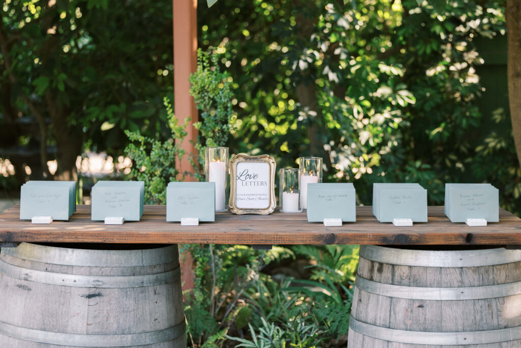 Gerry Ranch Reception Seating Chart Table - A rustic wooden table set on two barrels displays green envelopes, a 