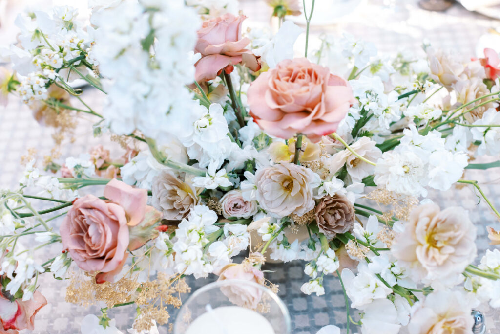 Oak Room Reception floral arrangement featuring blush pink and cream roses mixed with delicate white flowers and greenery, displayed on a light, patterned surface. Copyright - Lisa Leanne Photography, California
