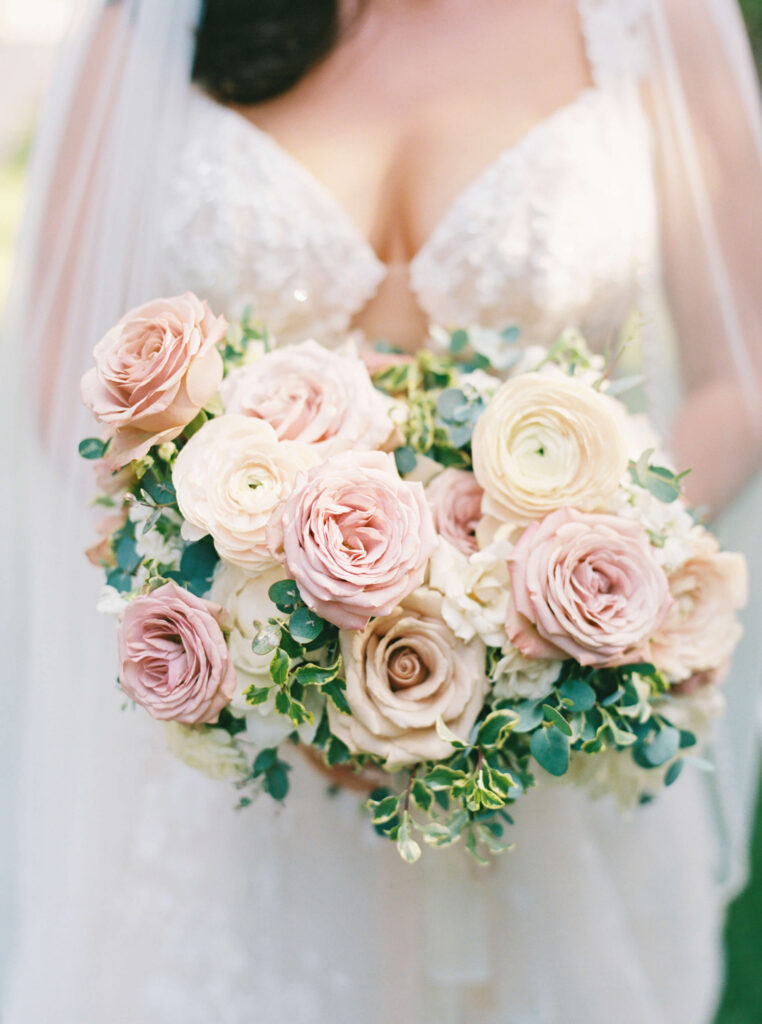 Villa Del Sol D'Oro Wedding Bridal Portrait - A bride in a white lace wedding dress holds a bouquet of large, pale pink and cream roses with green foliage. Copyright - Lisa Leanne Photography, California